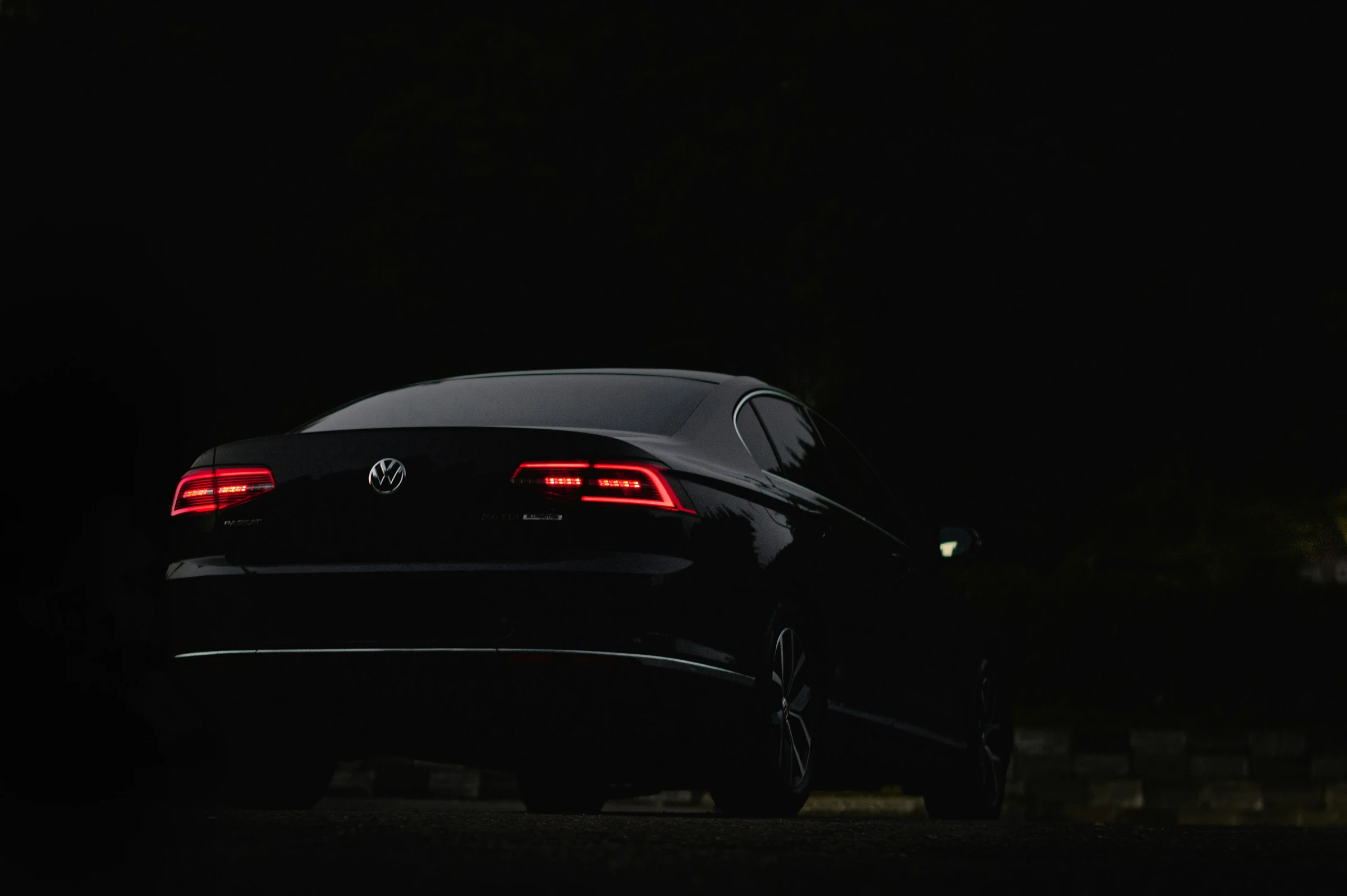 Rear of a dark Volkswagen saloon lit by its tail lights at night