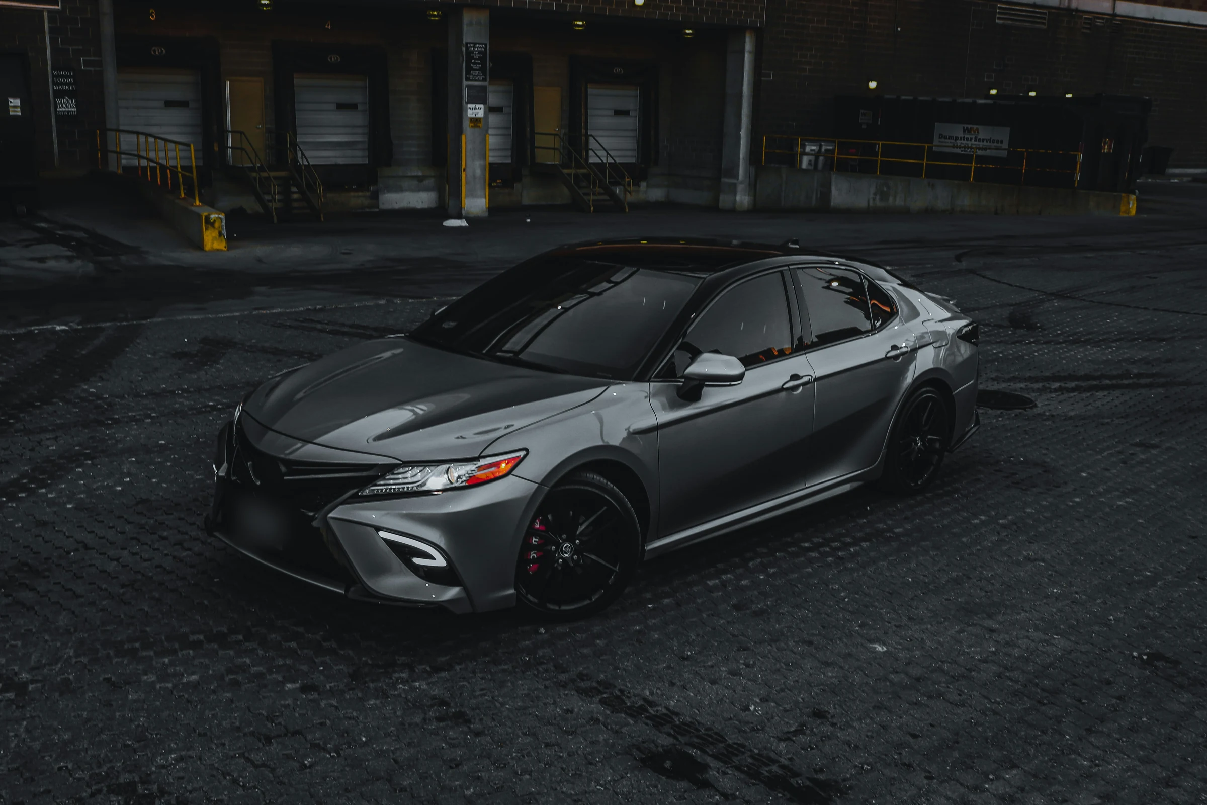 Grey Toyota Camry on wet cobbles by a loading bay