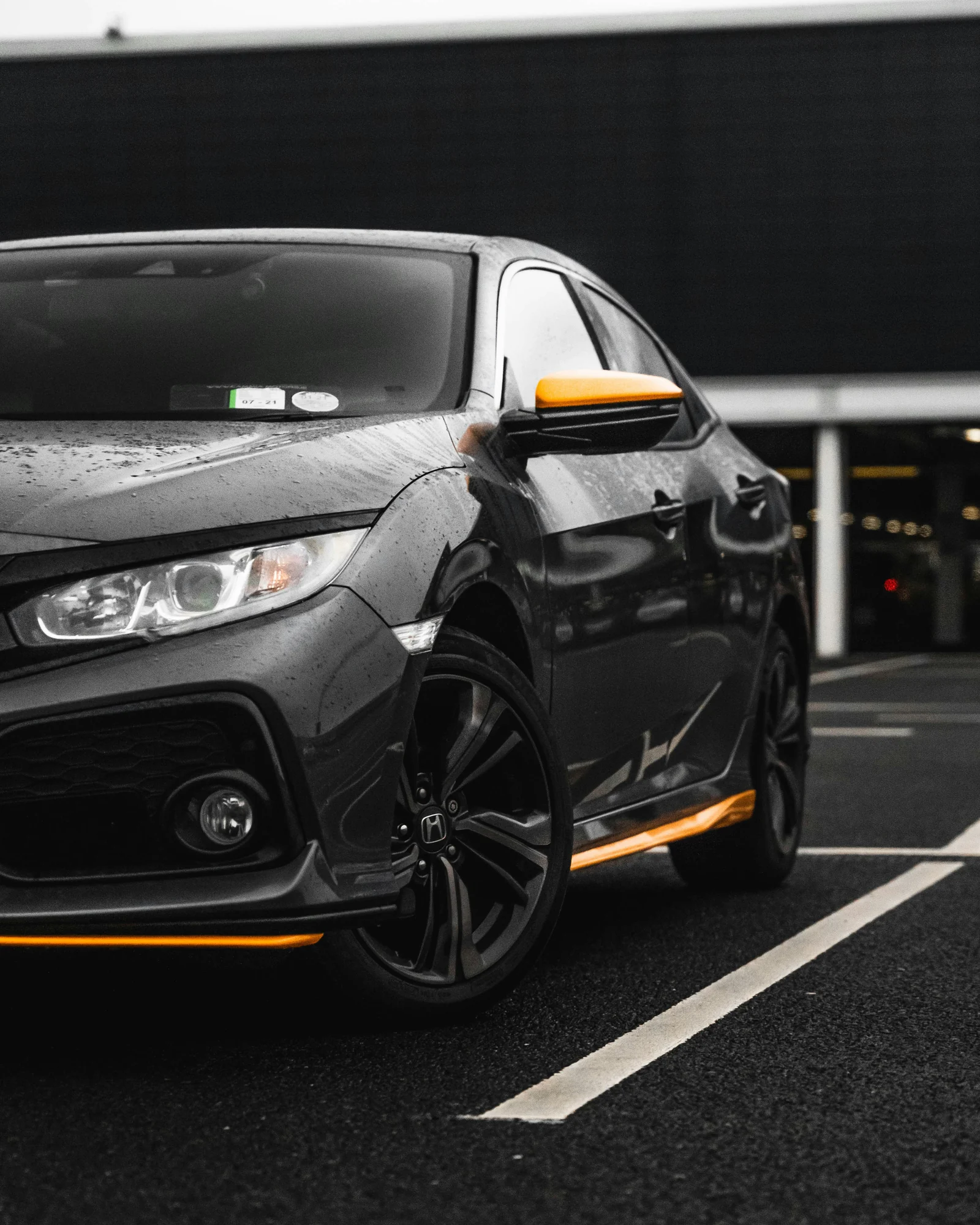 Front wing and alloy wheel of a black Honda Civic on wet ground